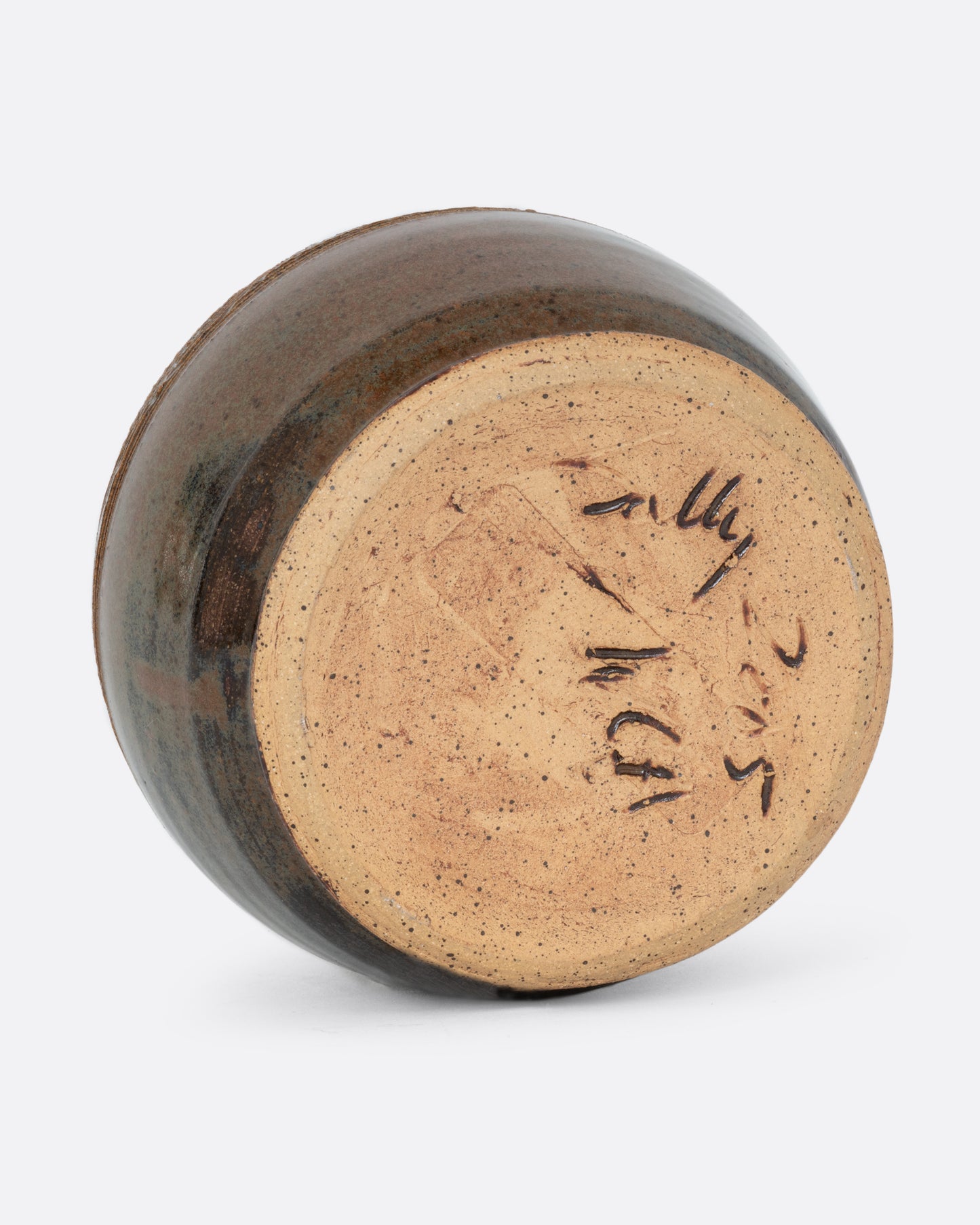 A round vase with a brown glaze and artist signed bottom. Shown on its side from the bottom.