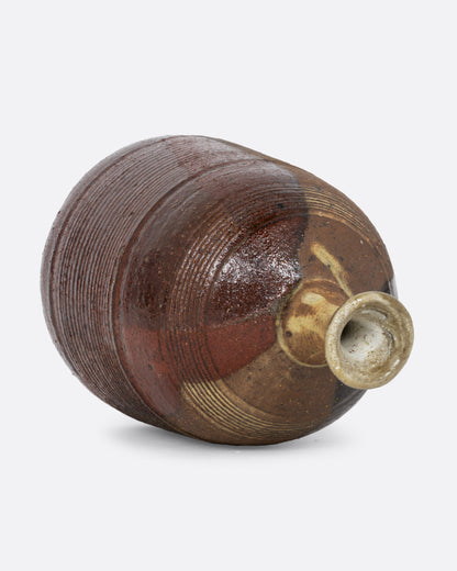 A vase with a brown split contrast glaze and ribbed texture. Shown diagonally on its side from the top.