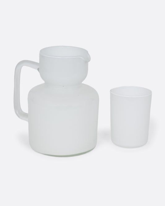 A white cased glass pitcher and matching cup. Shown from the side.