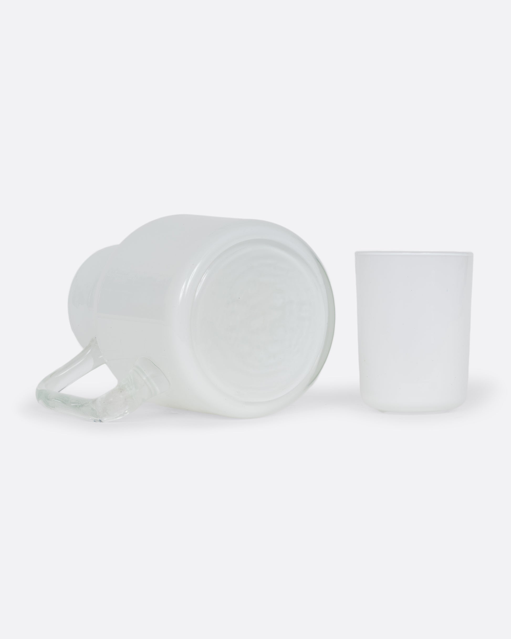 A white cased glass pitcher and matching cup. The pitcher is shown on its side from the bottom. The cup is shown from the front.
