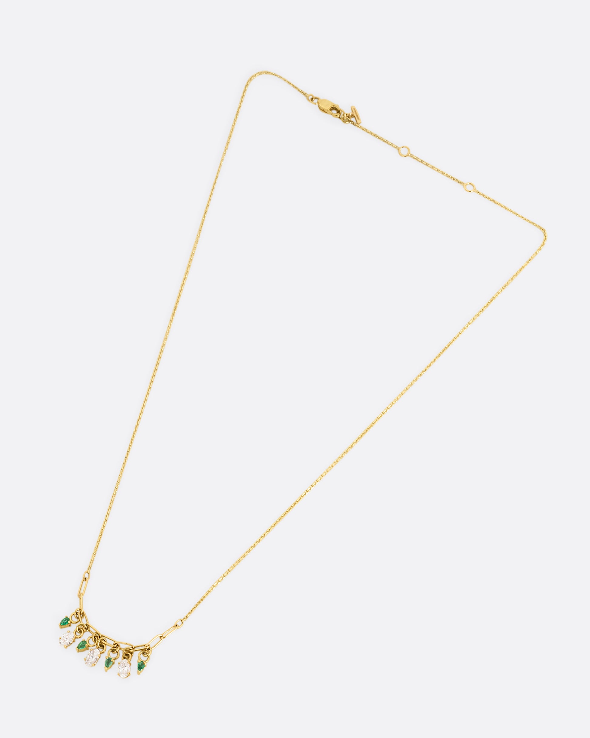 A yellow gold cable chain necklace with a paperclip chain section and diamonds and emeralds charms. Shown lying flat clasped.