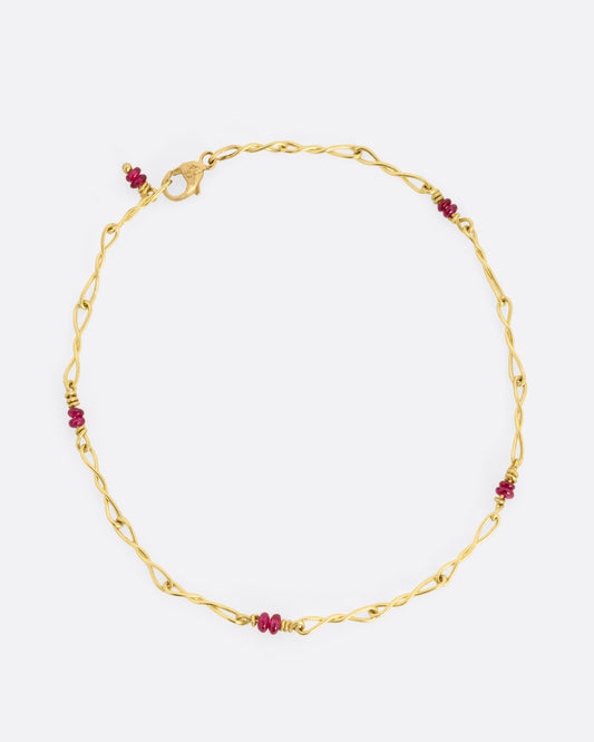 A yellow gold twisted paperclip chain link bracelet with five ruby beads.Shown clasped from the top.