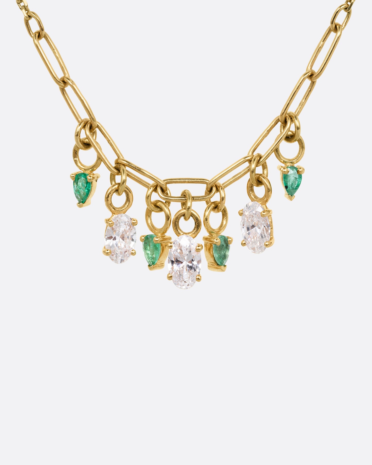 A yellow gold cable chain necklace with a paperclip chain section and diamonds and emeralds charms. Shown from the front.