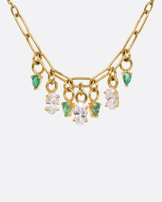 A yellow gold cable chain necklace with a paperclip chain section and diamonds and emeralds charms. Shown from the front.