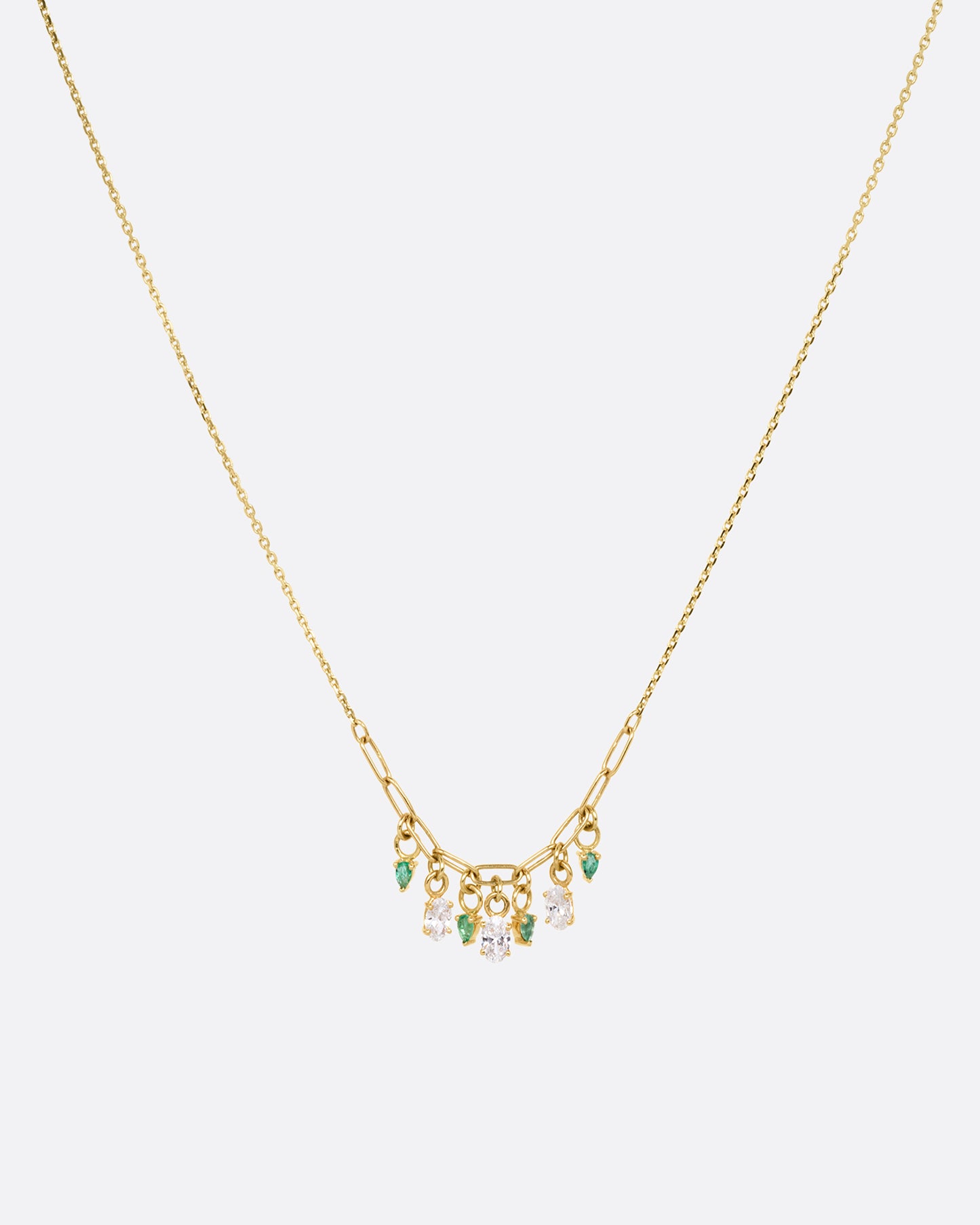 A yellow gold cable chain necklace with a paperclip chain section and diamonds and emeralds charms. Shown from the front.