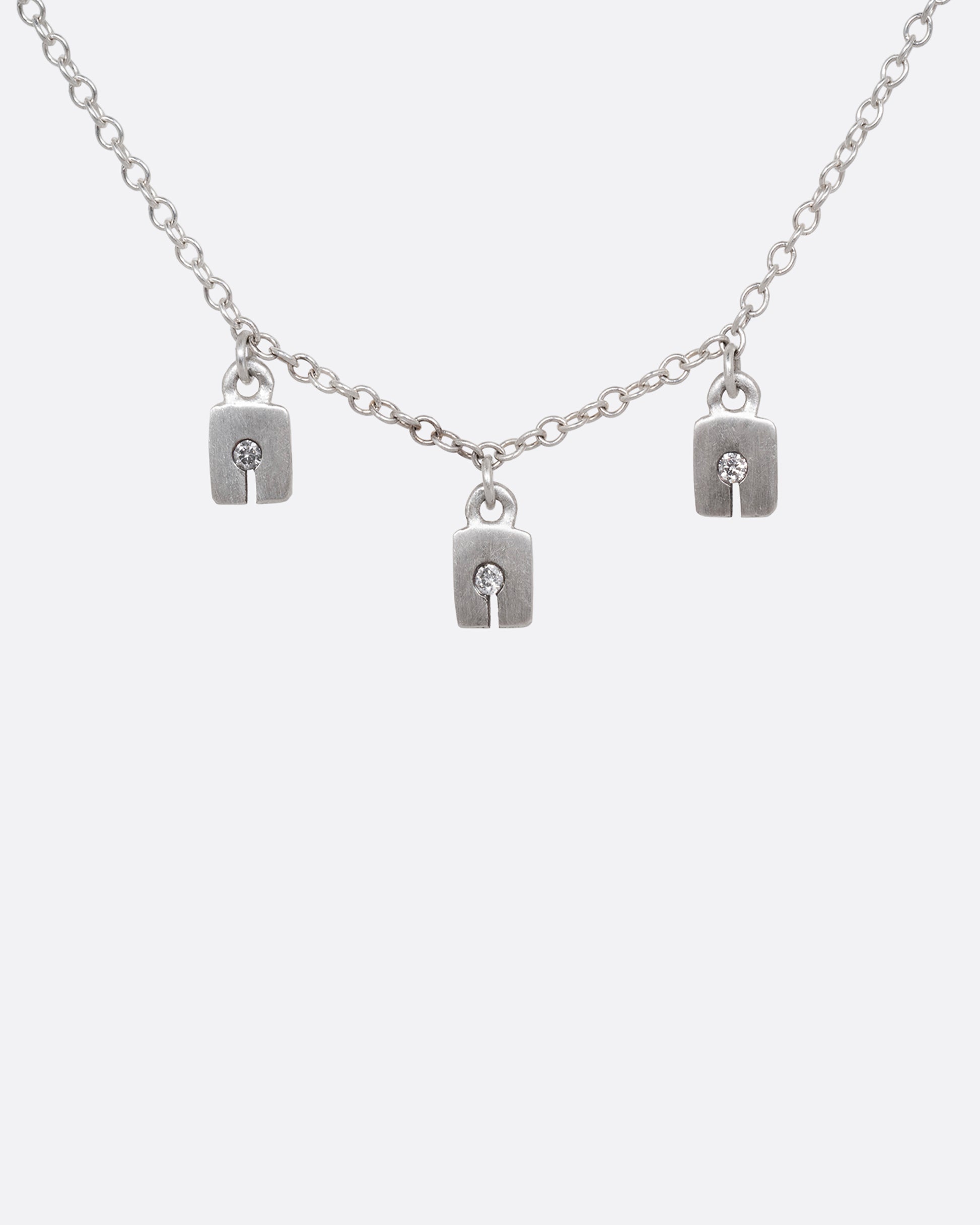 A silver cable chain necklace with three square charms with grey diamonds. Shown from the front.