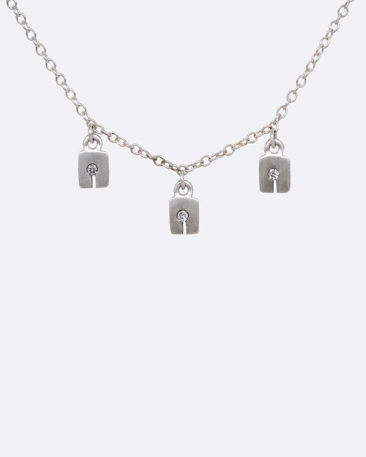 A silver cable chain necklace with three square charms with grey diamonds. Shown from the front.