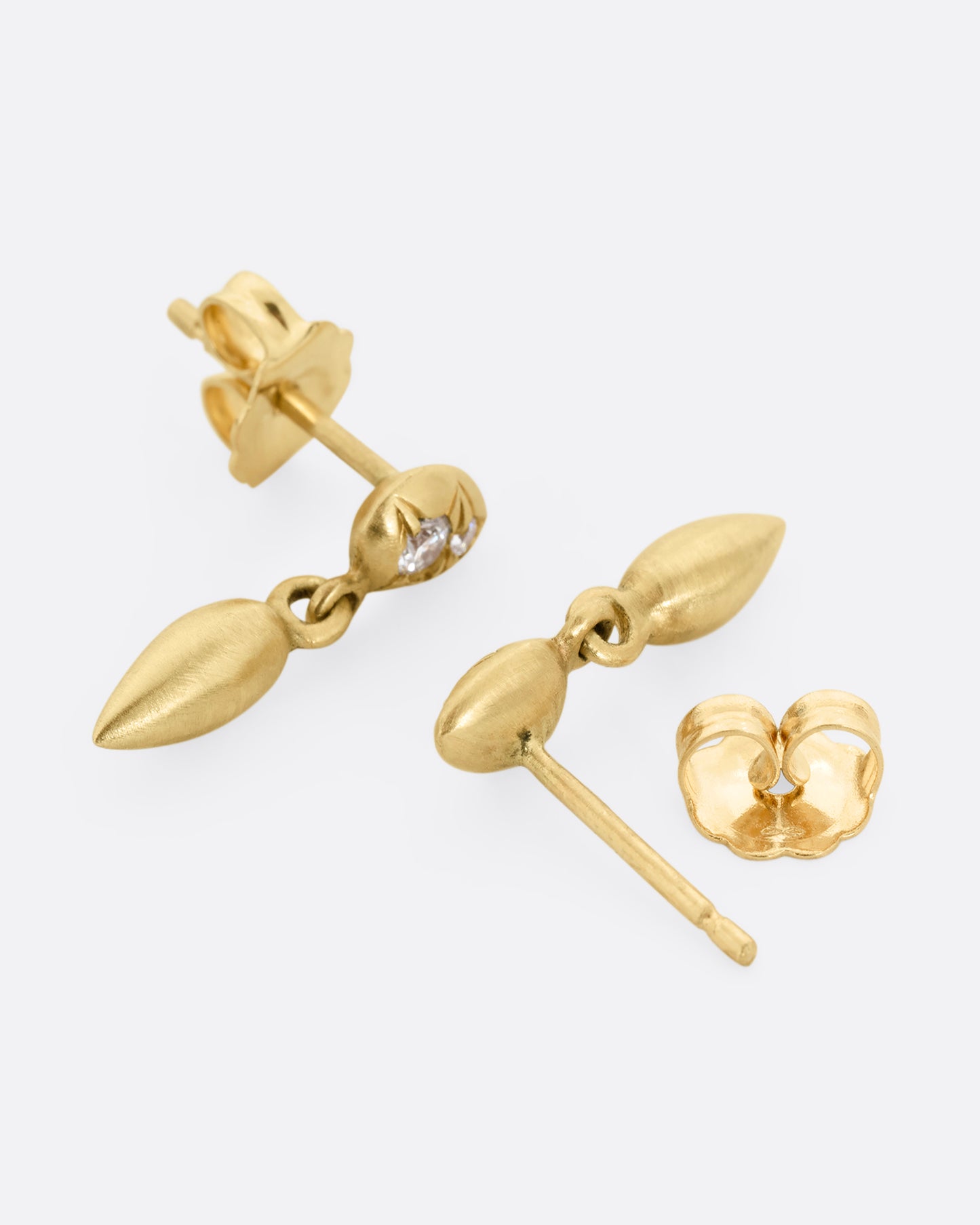 Yellow gold diamond earrings with teardrop shaped dangles. One earring is shown lying flat from the bottom. The other earring is shown lying flat open from the top.