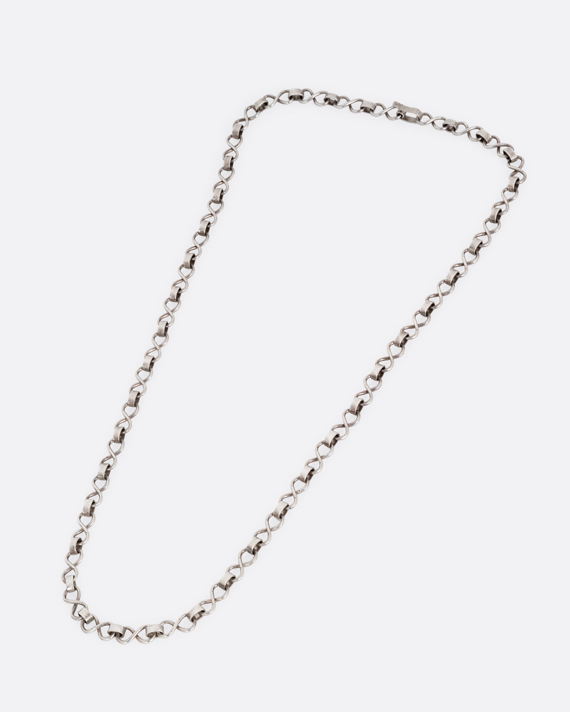 A silver  infinity link necklace. Shown lying flat diagonally from the front.