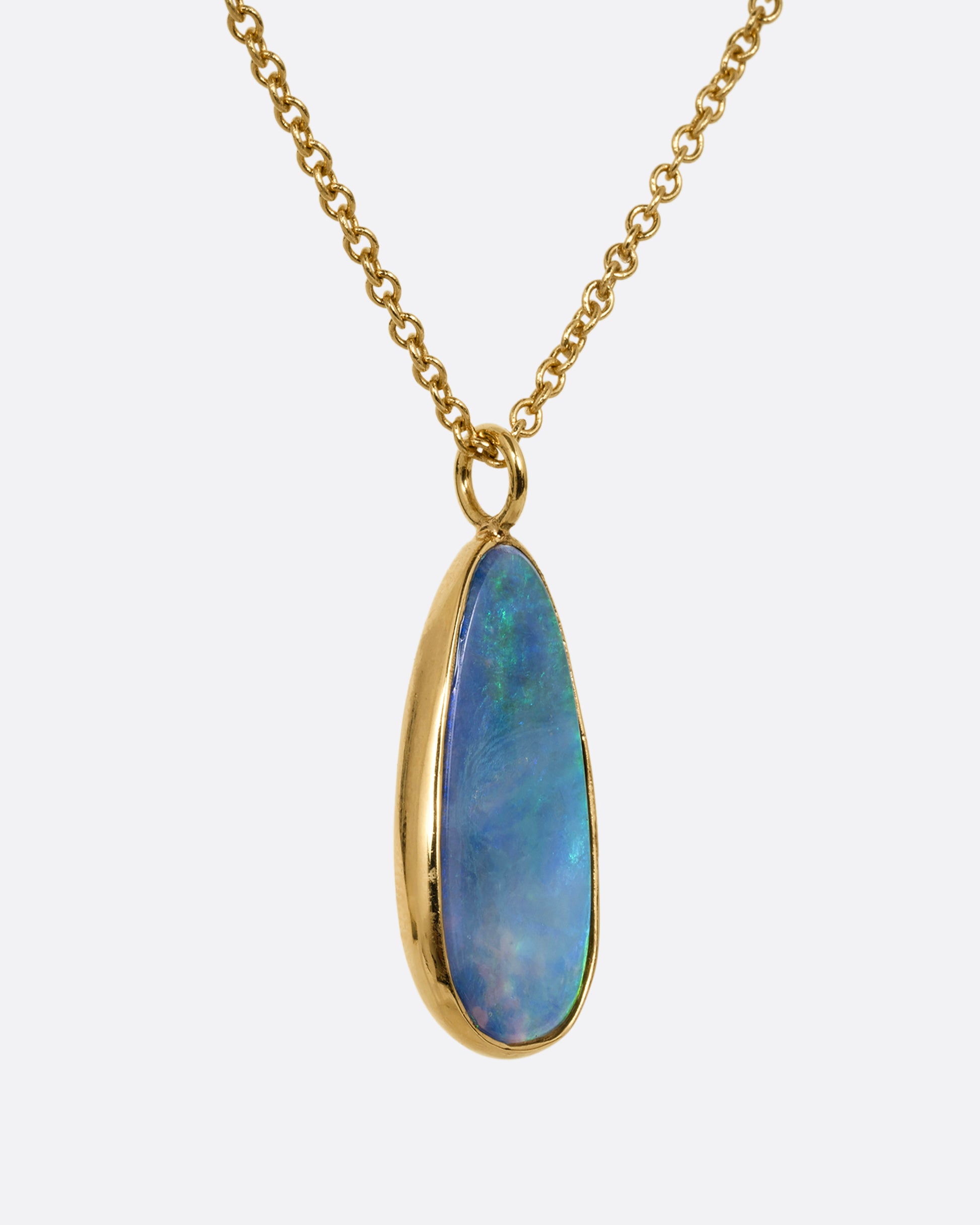 An opal pendant set in yellow gold hanging from a yellow gold cable chain. Shown from the side.