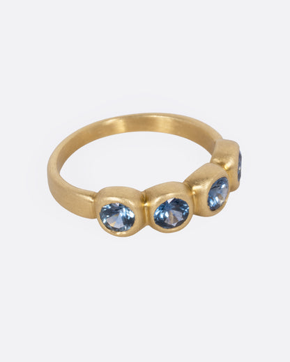 A yellow gold ring with four blue sapphires, shown from the side.