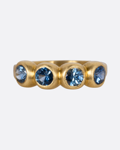 A yellow gold ring with four blue sapphires, shown from the front.