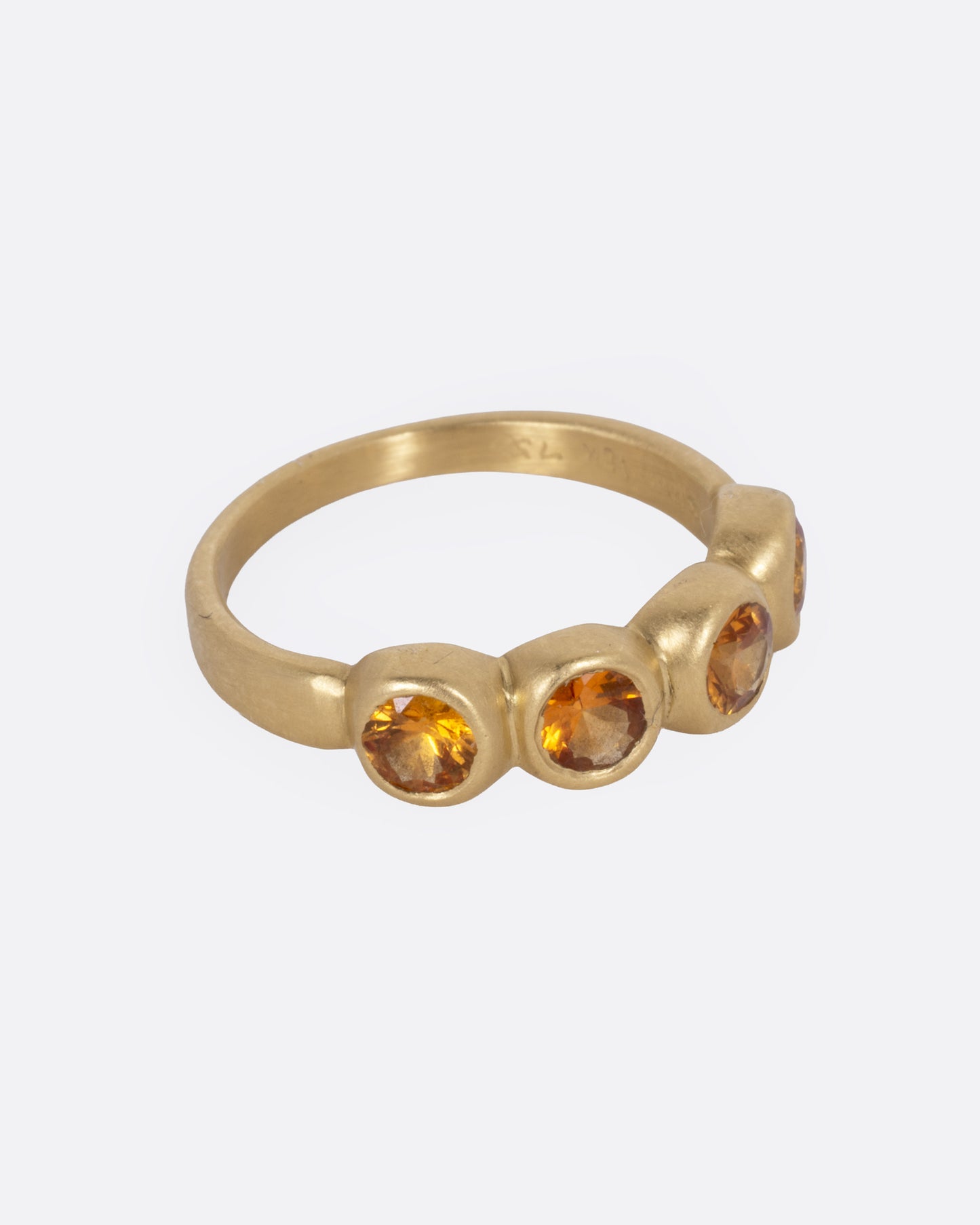 A yellow gold ring with four bezel set orange sapphires, shown from the side.