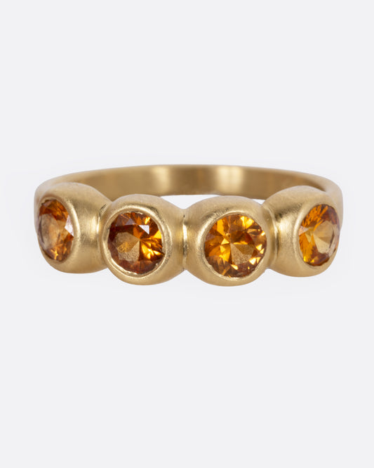 A yellow gold ring with four bezel set orange sapphires, shown from the front.