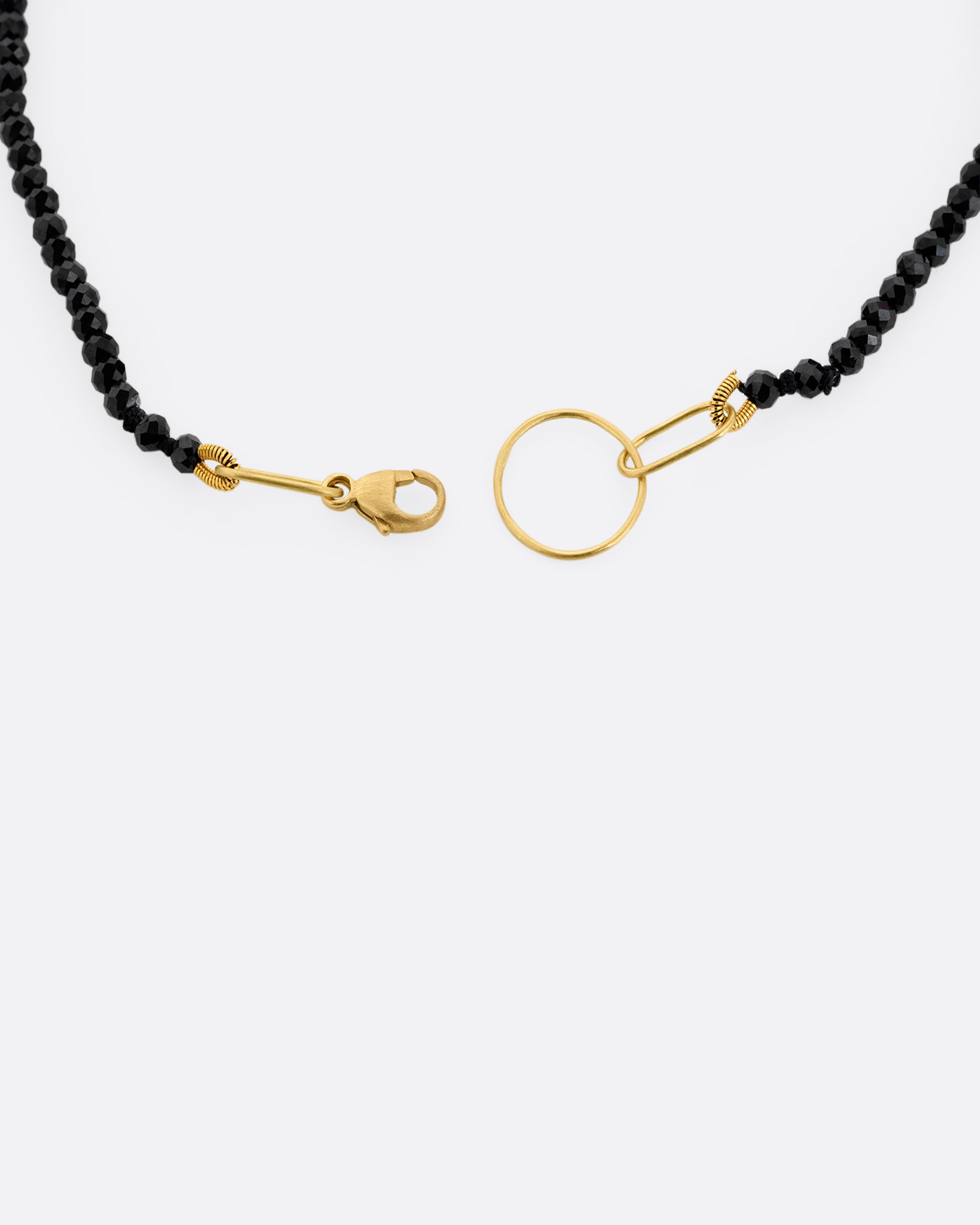 A close up of a black spinel beaded bracelet with a yellow gold clasp. 