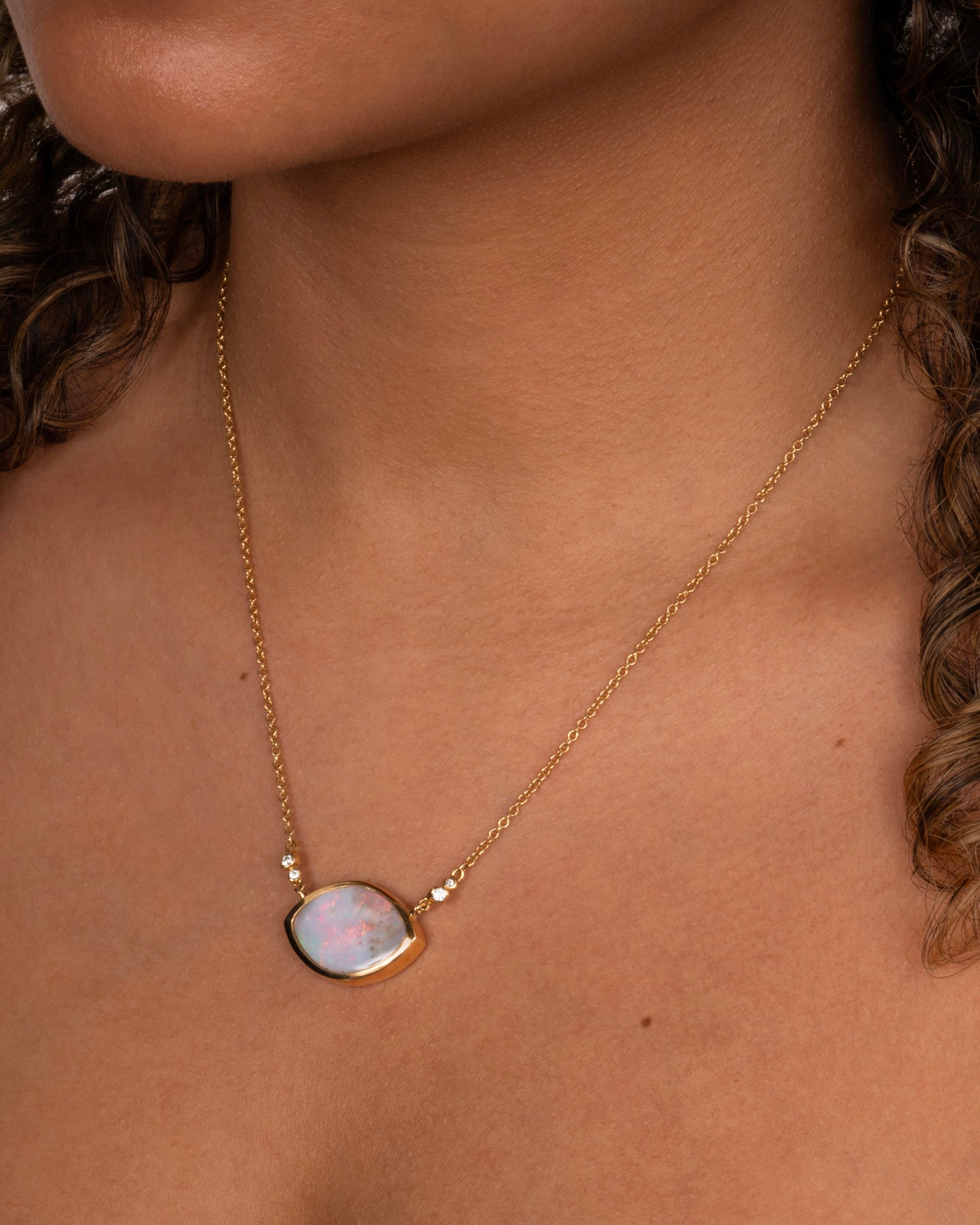 A yellow gold cable chain necklace with a large eye shaped opal pendant and diamond accents. Shown worn around the neck.