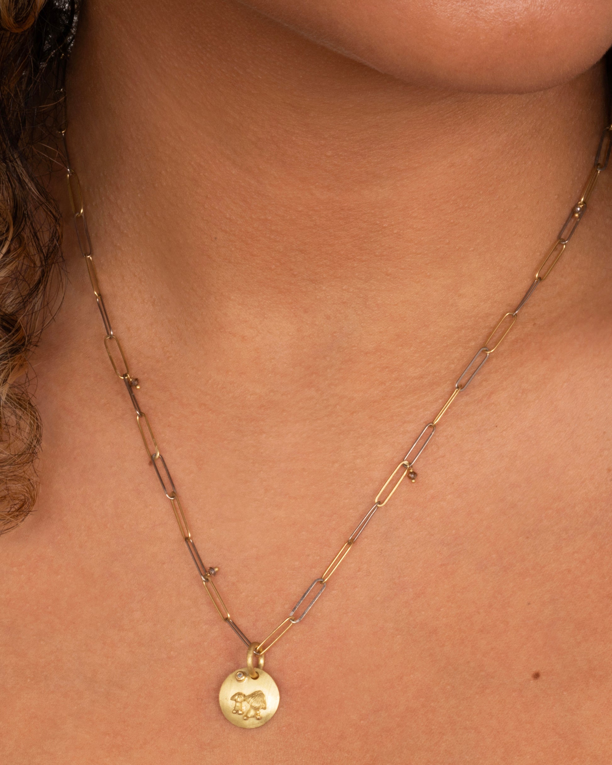 A yellow gold medallion with a diamond and mushrooms. Shown worn around the neck.