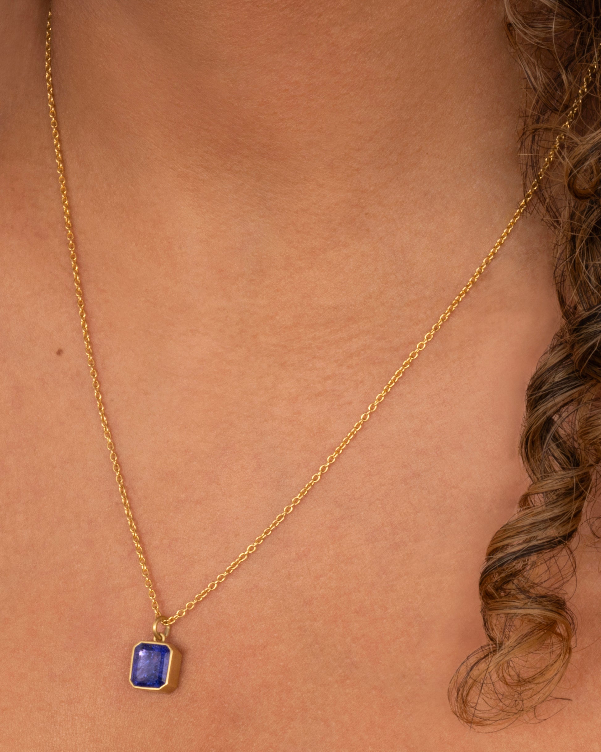 yellow gold necklace with an emerald cut tanzanite shown worn around the neck.