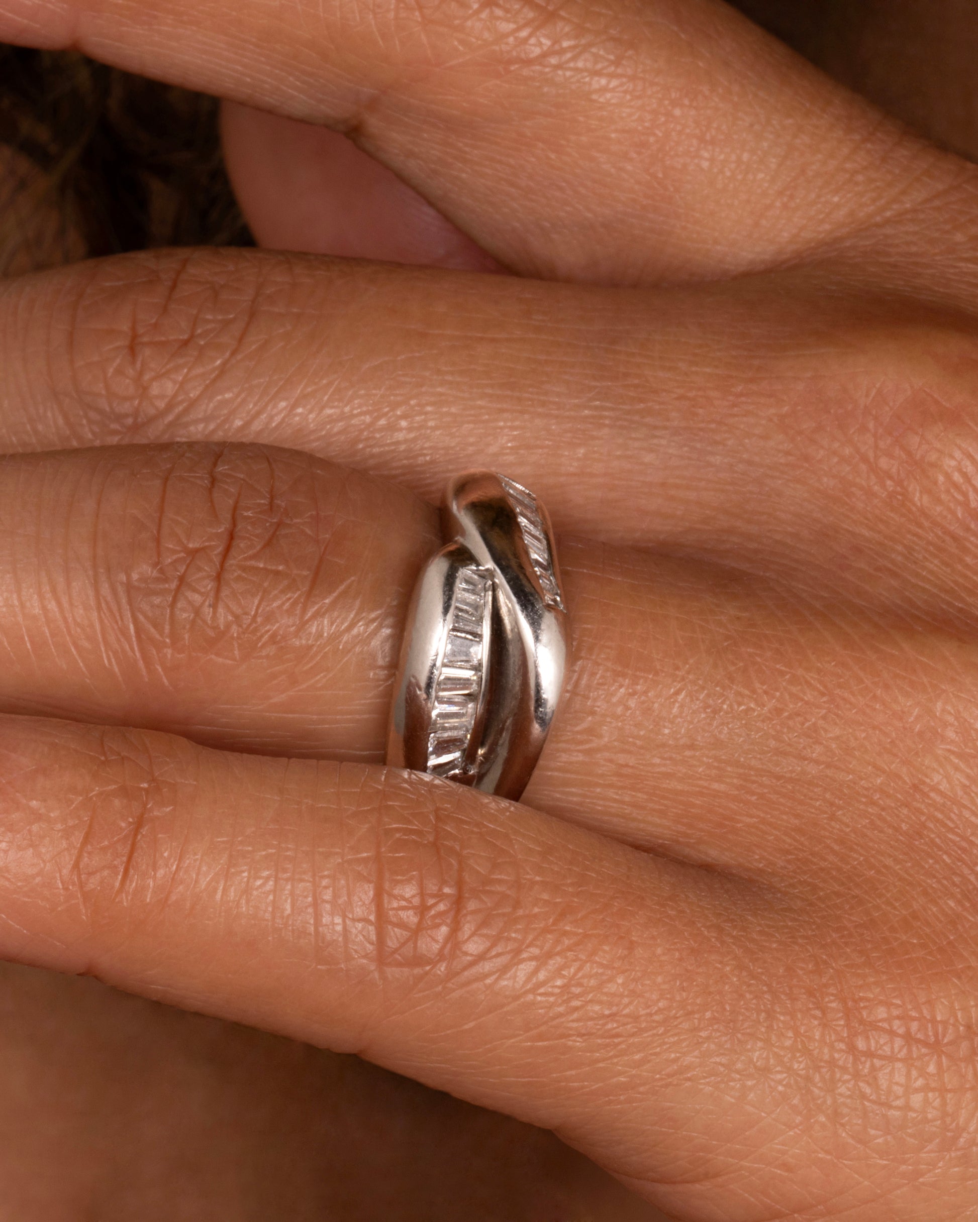 A platinum ring with two arches, lined with baguette diamonds. shown on a finger.