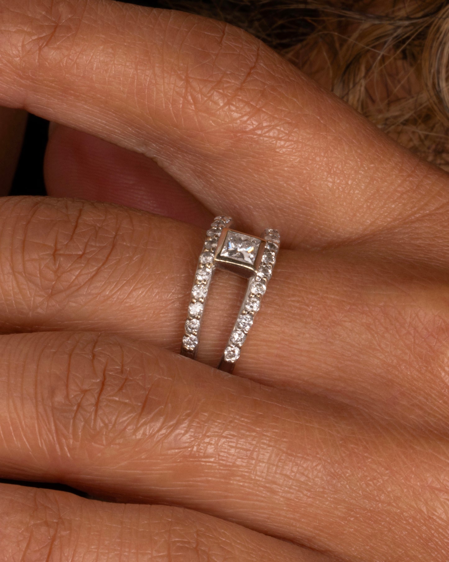 A yellow and white gold double band with pave diamonds and a center princess cut diamond. Shown worn on a hand.