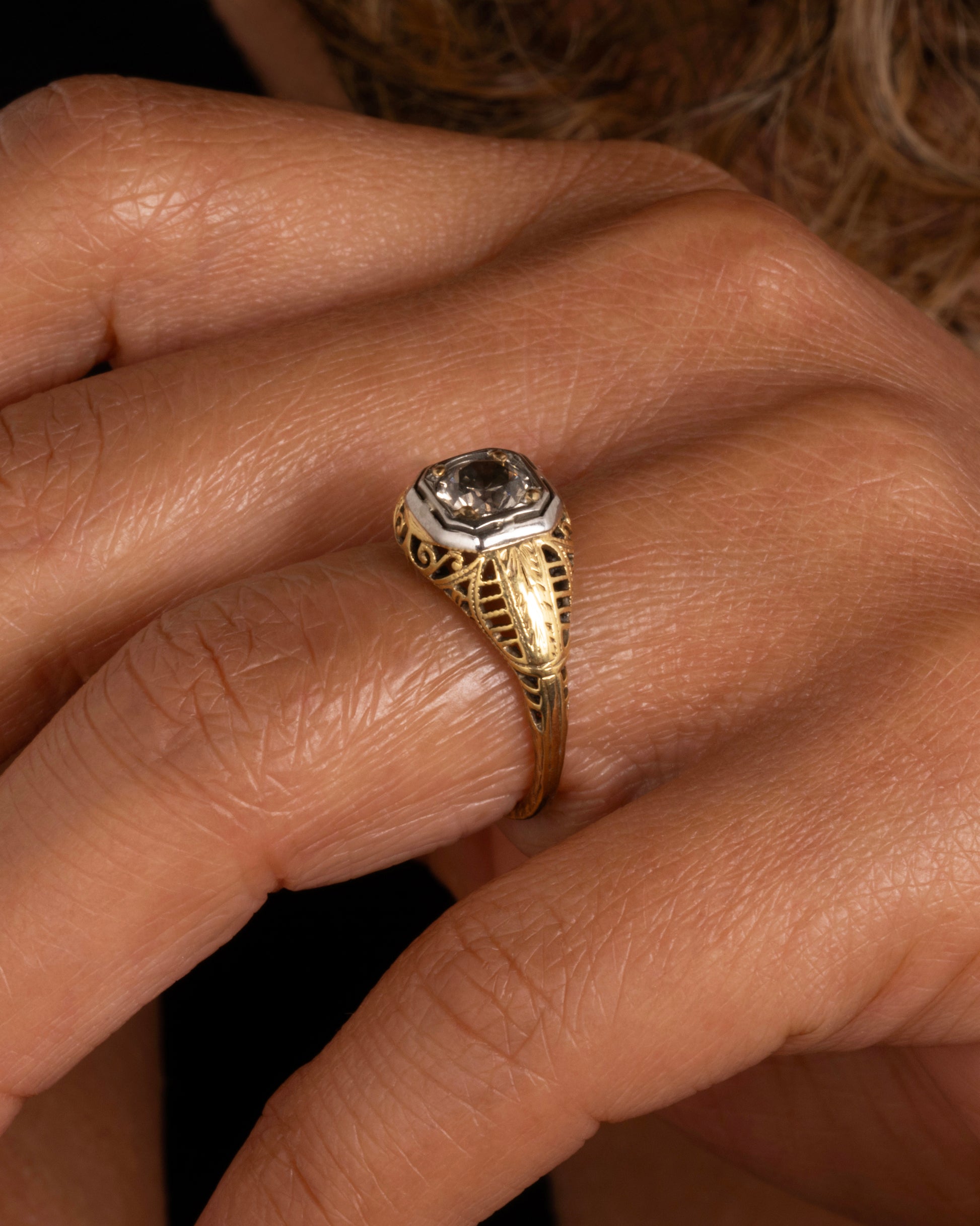 A filigree-covered signet ring with a champagne diamond at its center, set in a white gold bezel.