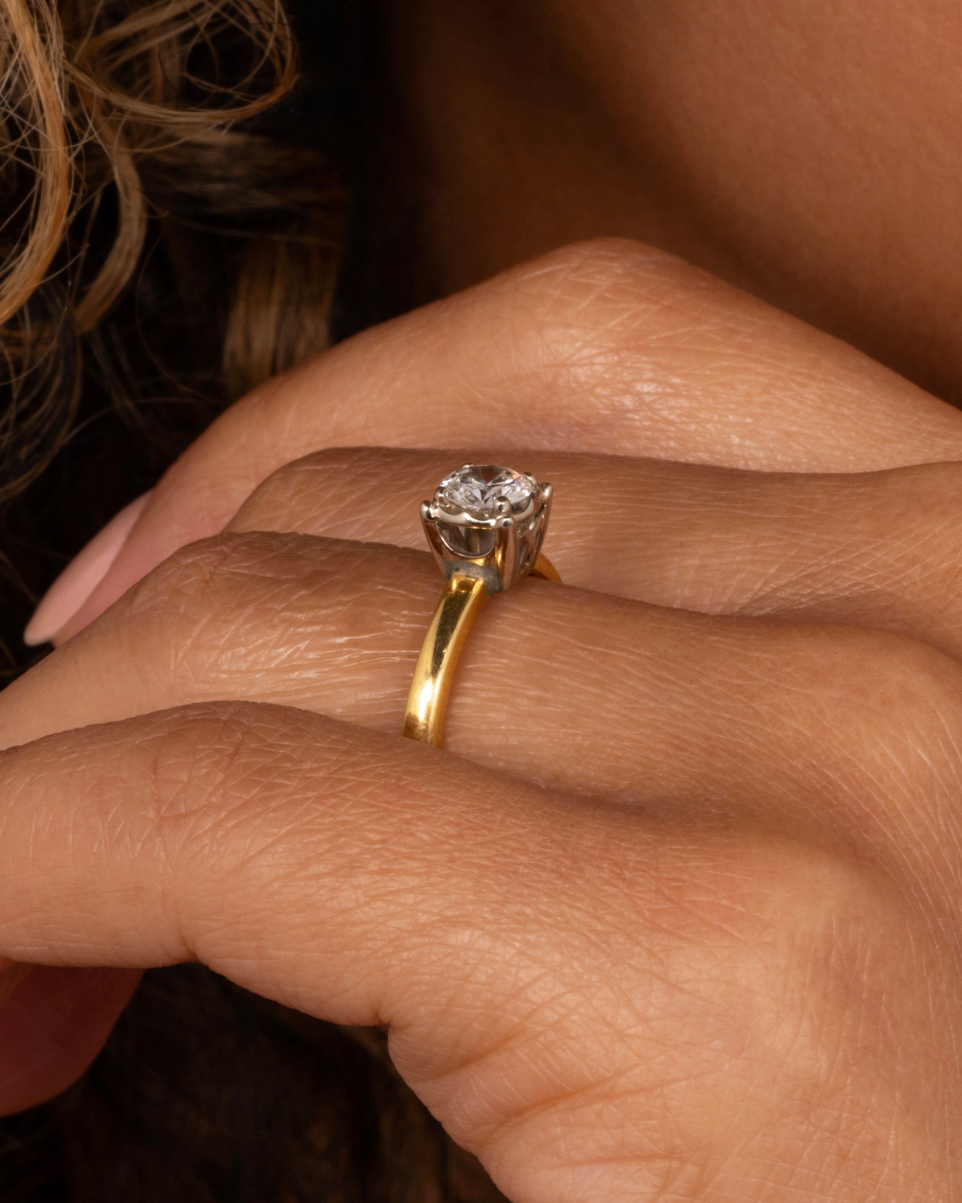 A yellow gold ring with a white gold prong setting and a brilliant cut diamond. Shown worn on a finger.