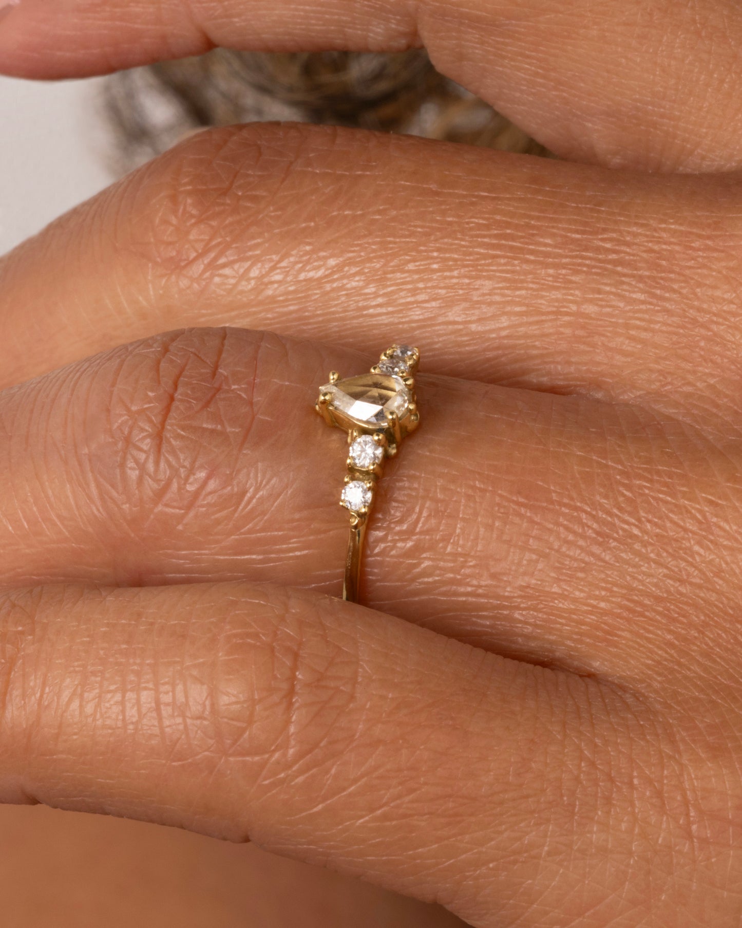  A yellow gold ring with a pear shaped champagne diamond with round white diamond accents. Shown on a hand.