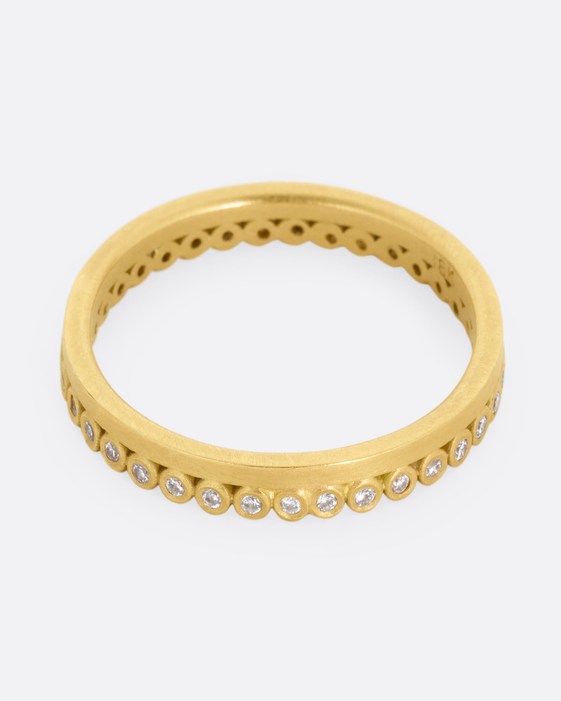 A yellow gold ring with bezel set diamond dots encircling one side. Shown from the top.