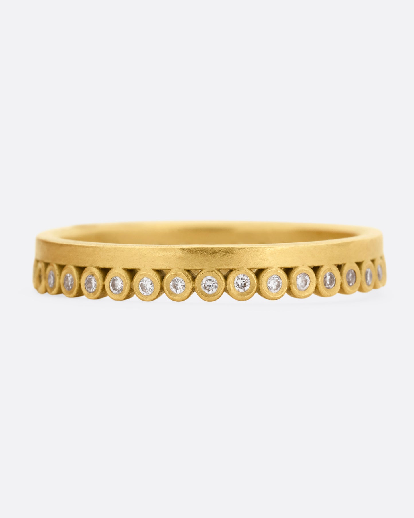 A yellow gold ring with bezel set diamond dots encircling one side. Shown from the front.