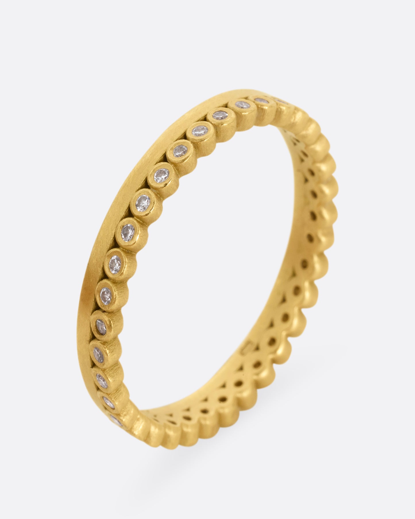 A yellow gold ring with bezel set diamond dots encircling one side. Shown standing up from the front.