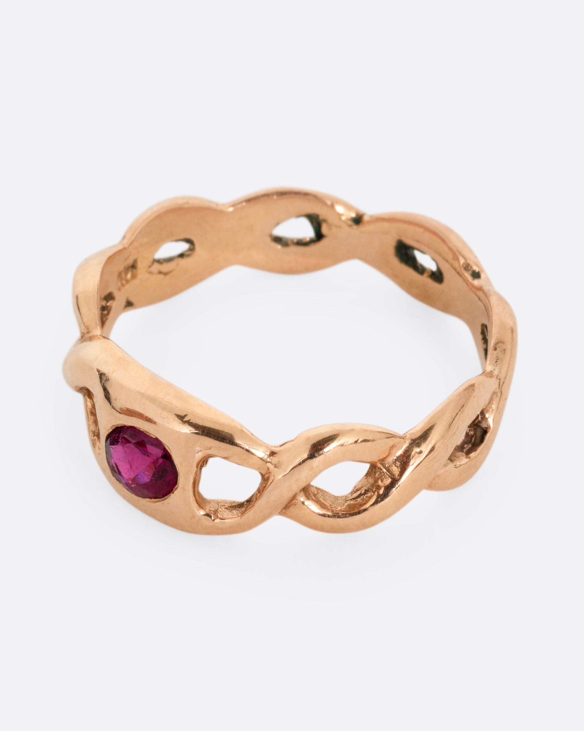 A rose gold ring with a twisted motif and pink tourmaline at the center. Shown from the side.