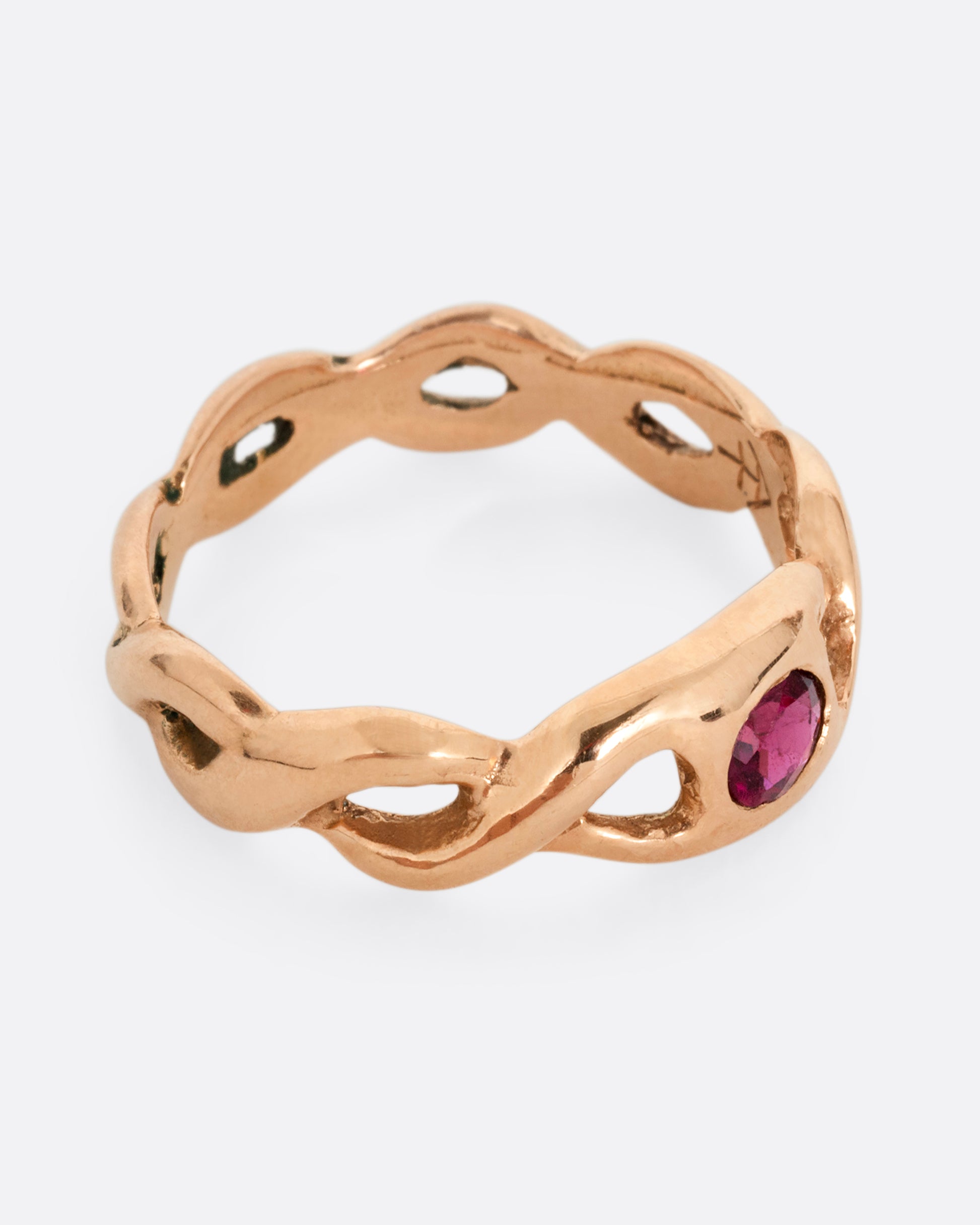 A rose gold ring with a twisted motif and pink tourmaline at the center. Shown from the side.