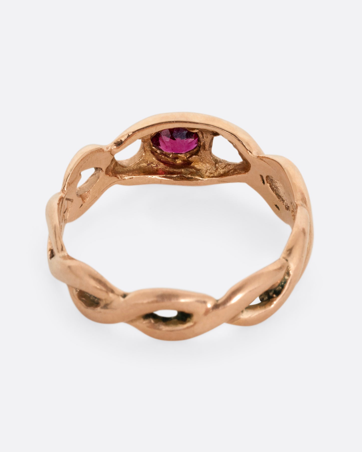 A rose gold ring with a twisted motif and pink tourmaline at the center. Shown from the back.
