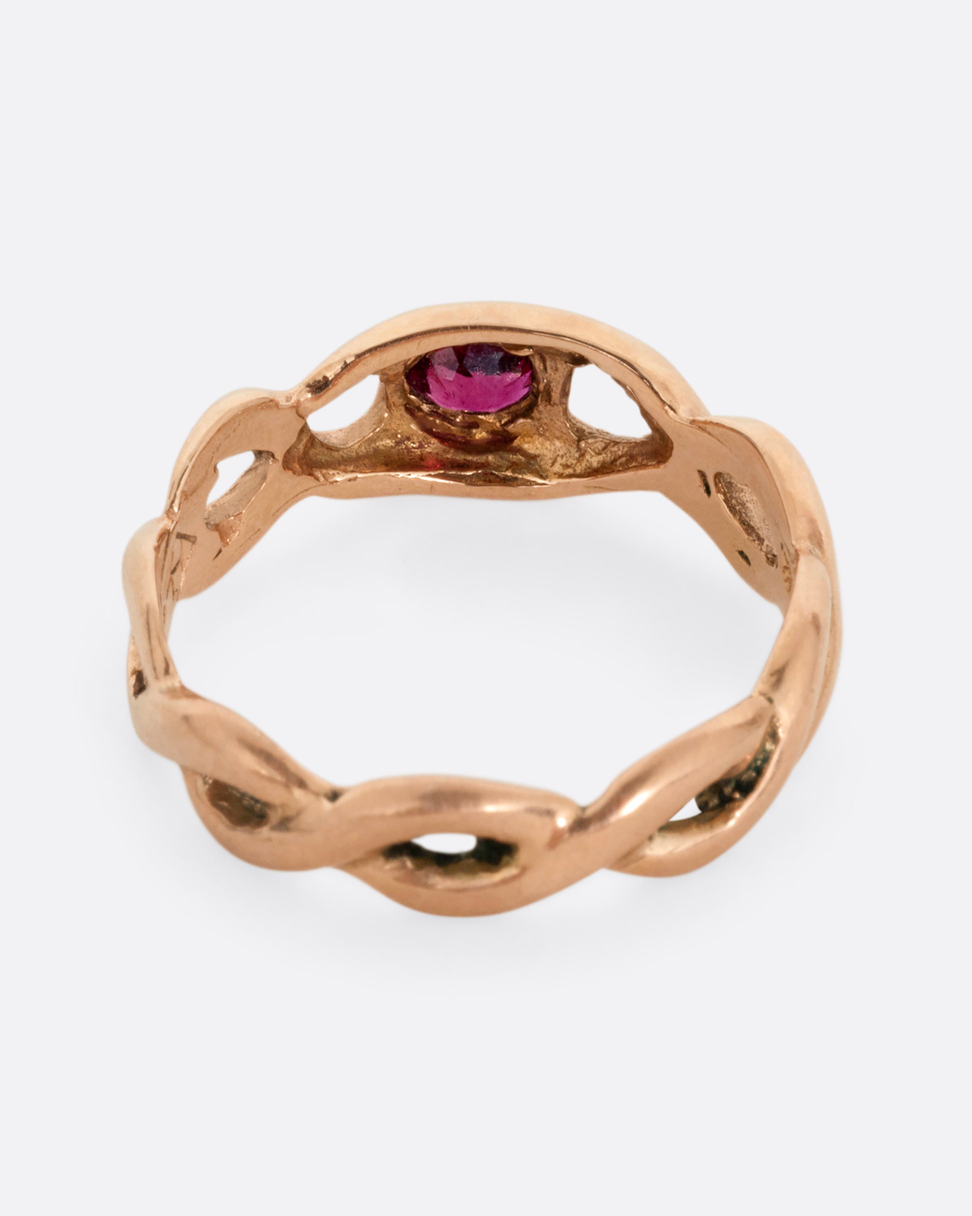A rose gold ring with a twisted motif and pink tourmaline at the center. Shown from the back.
