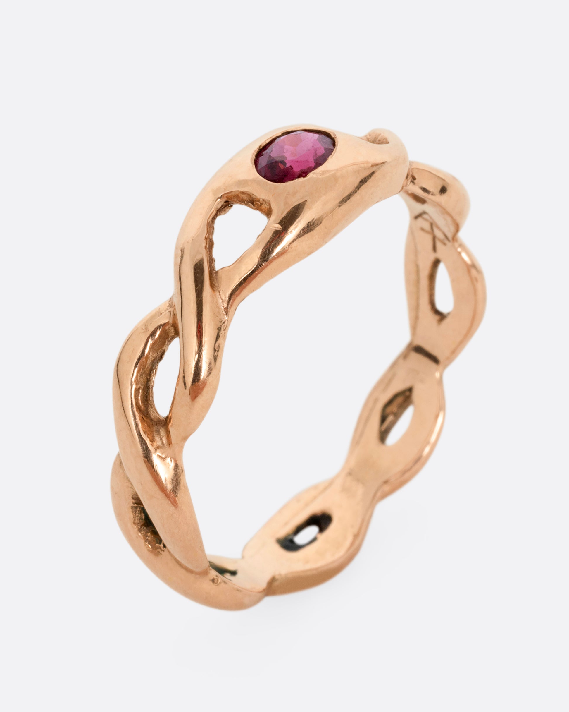A rose gold ring with a twisted motif and pink tourmaline at the center. Shown standing up from the side.