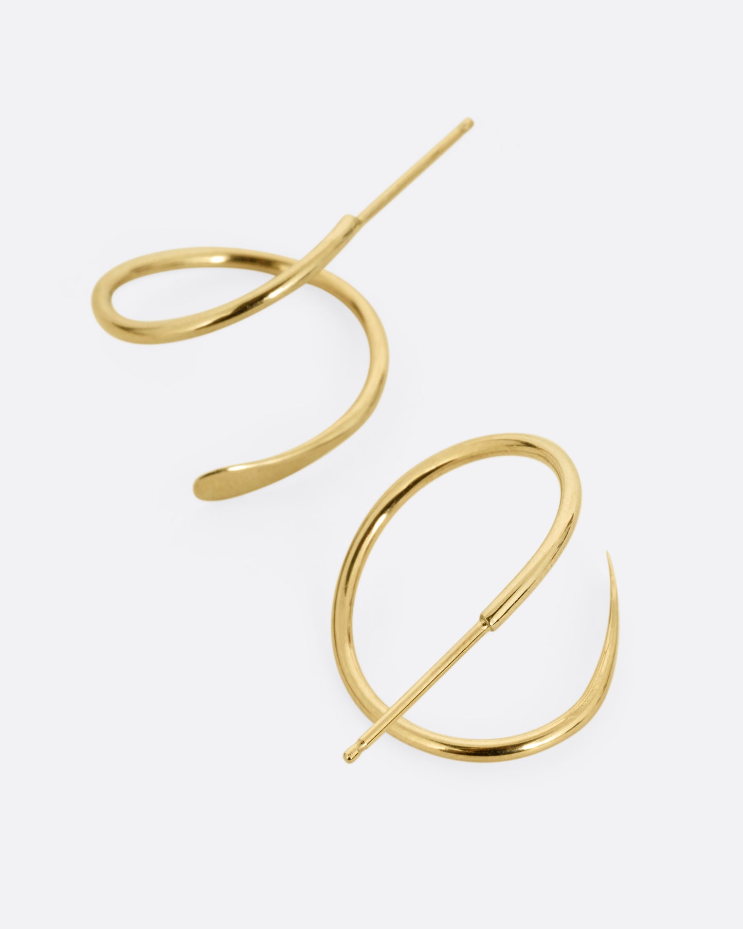 A pair of yellow gold earrings in a loop shape with one hammered flat end. Shown from the top.