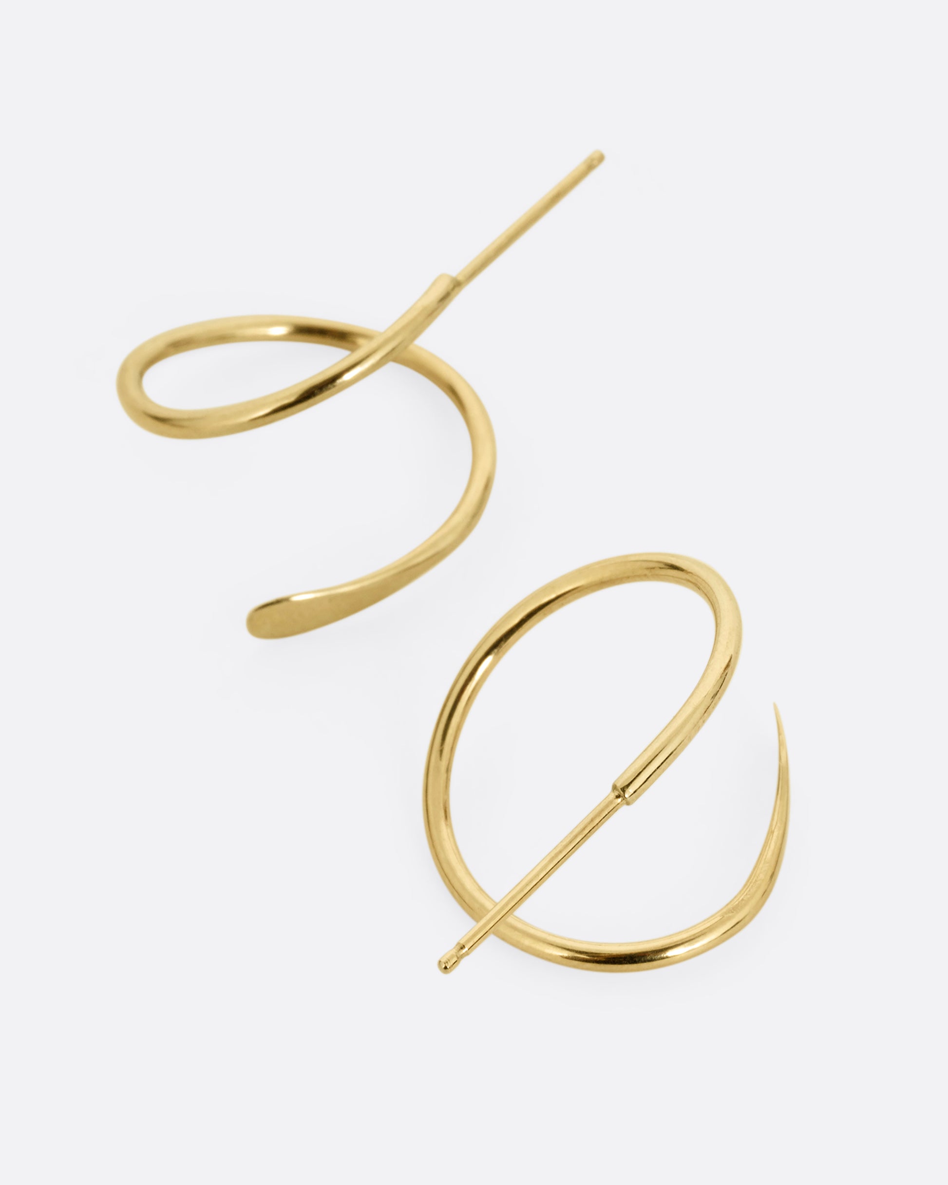 A pair of yellow gold earrings in a loop shape with one hammered flat end. Shown from the top.