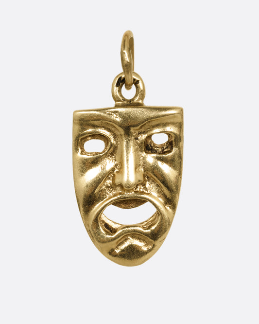 A yellow gold double sided theatrical mask charm. This side is frowning. Shown from the front.