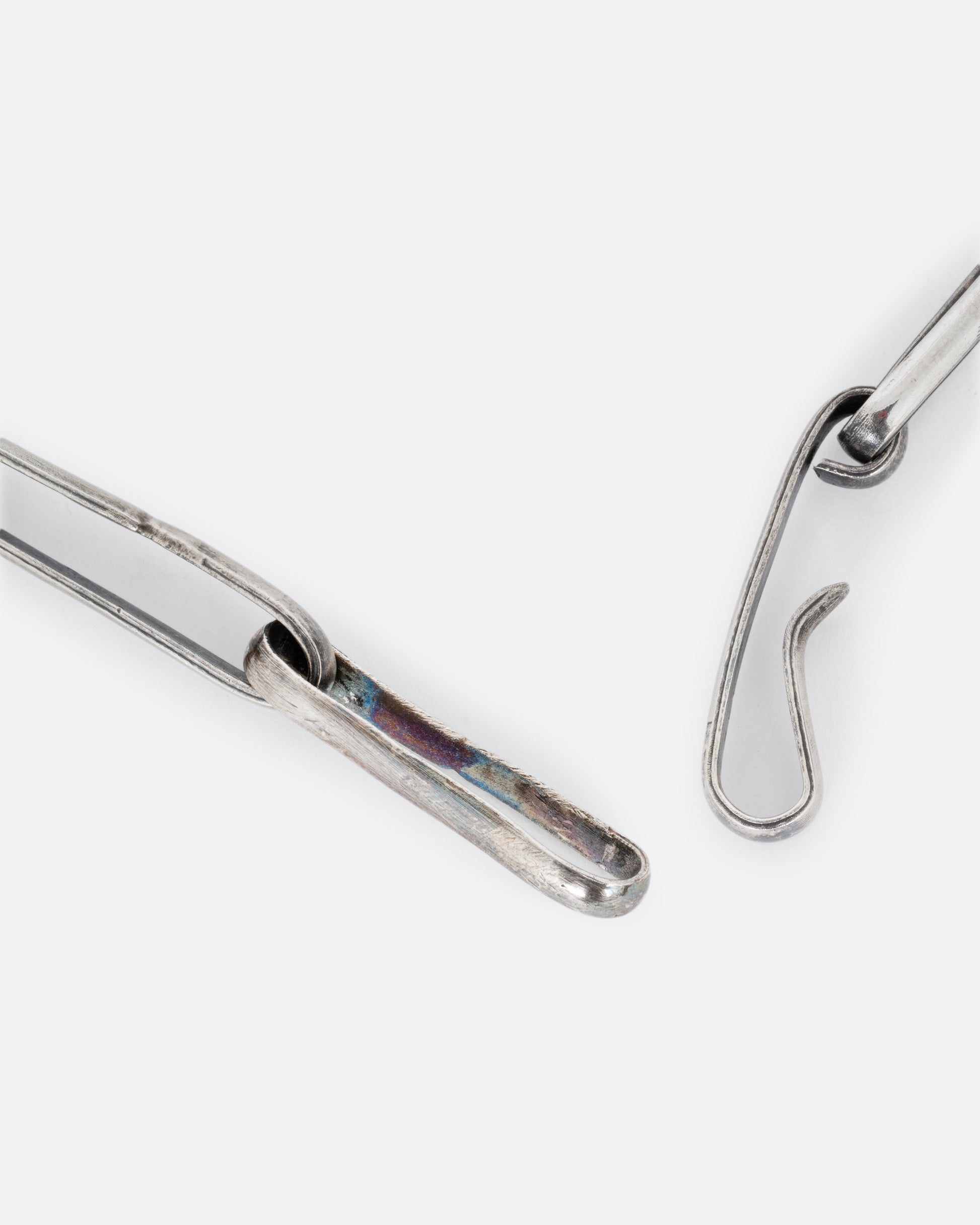 A close up of the clasp of a silver wide link cable chain necklace. Shown open.