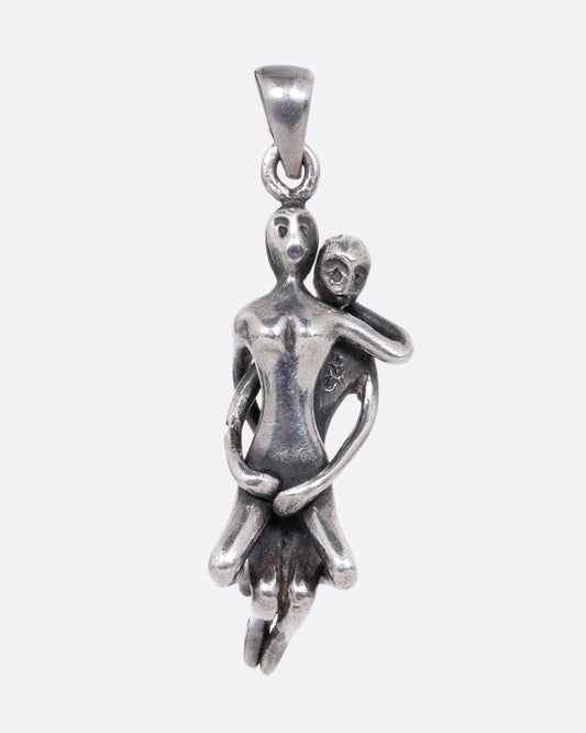 A silver pendant with two people embraced in an erotic position. Shown from the front.