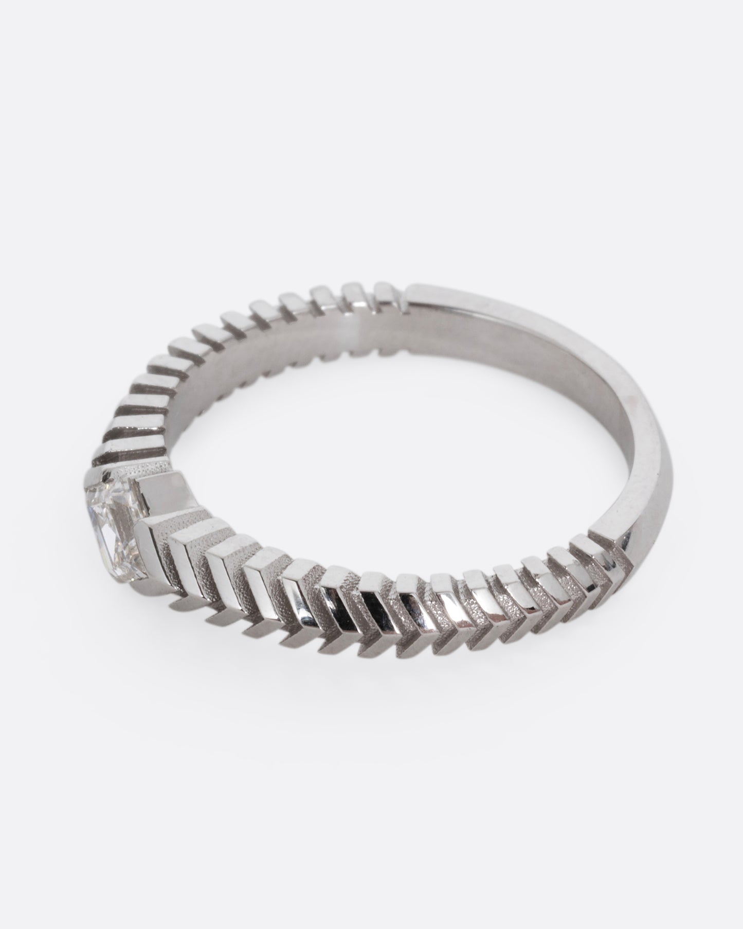 A platinum ring with a 'pleated' motif and lozenge shaped diamond at the center. Shown from the side.