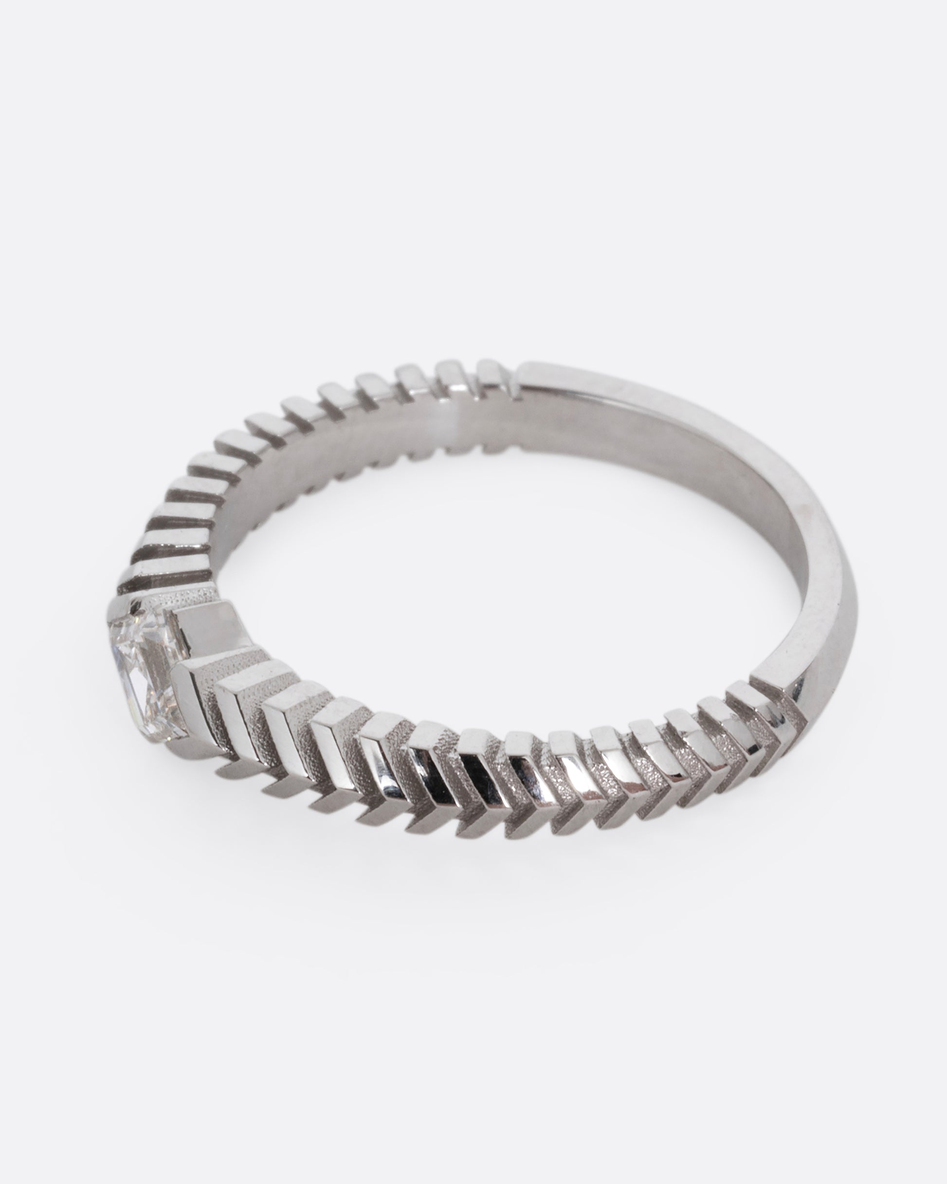 A platinum ring with a 'pleated' motif and lozenge shaped diamond at the center. Shown from the side.