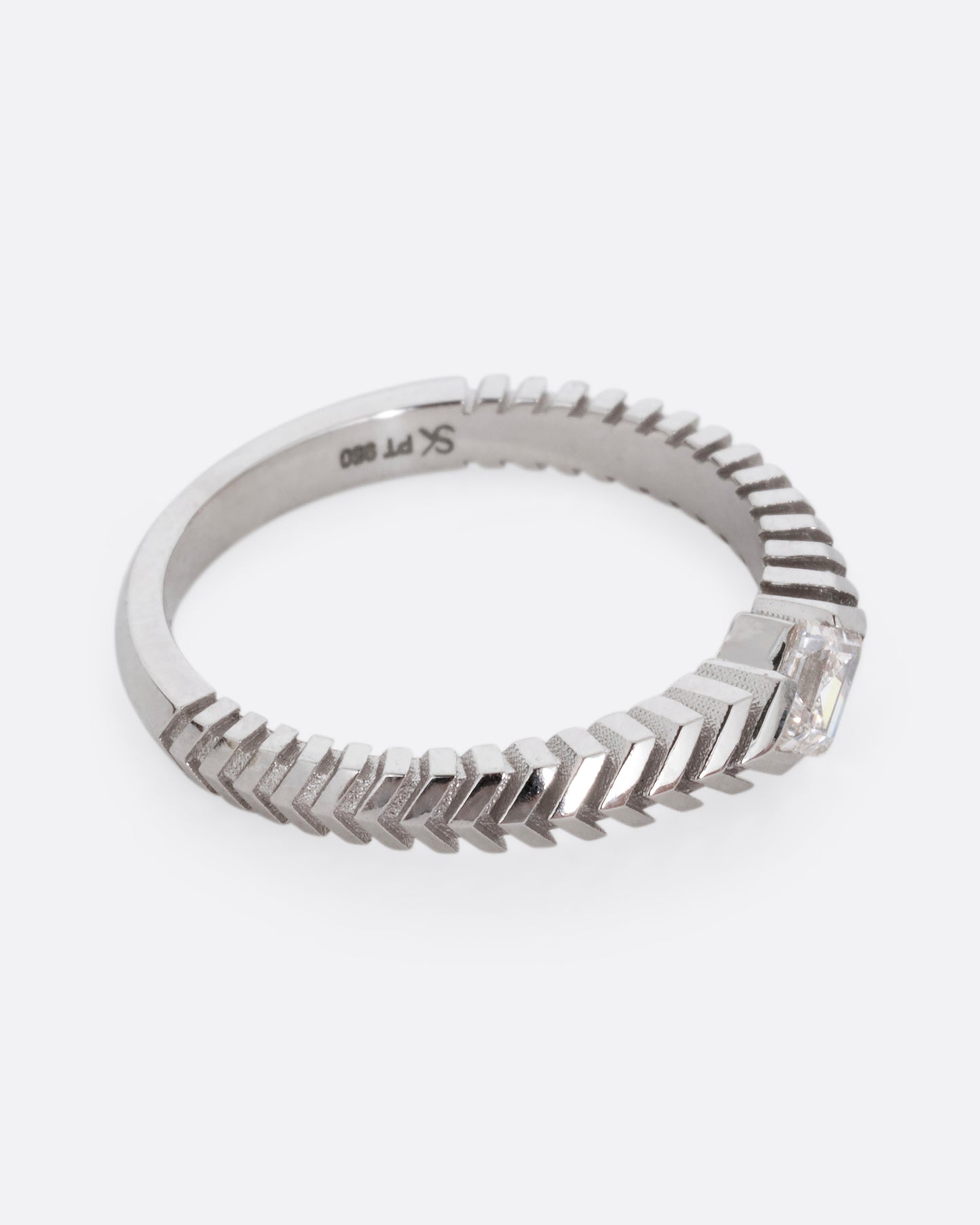 A platinum ring with a 'pleated' motif and lozenge shaped diamond at the center. Shown from the side.