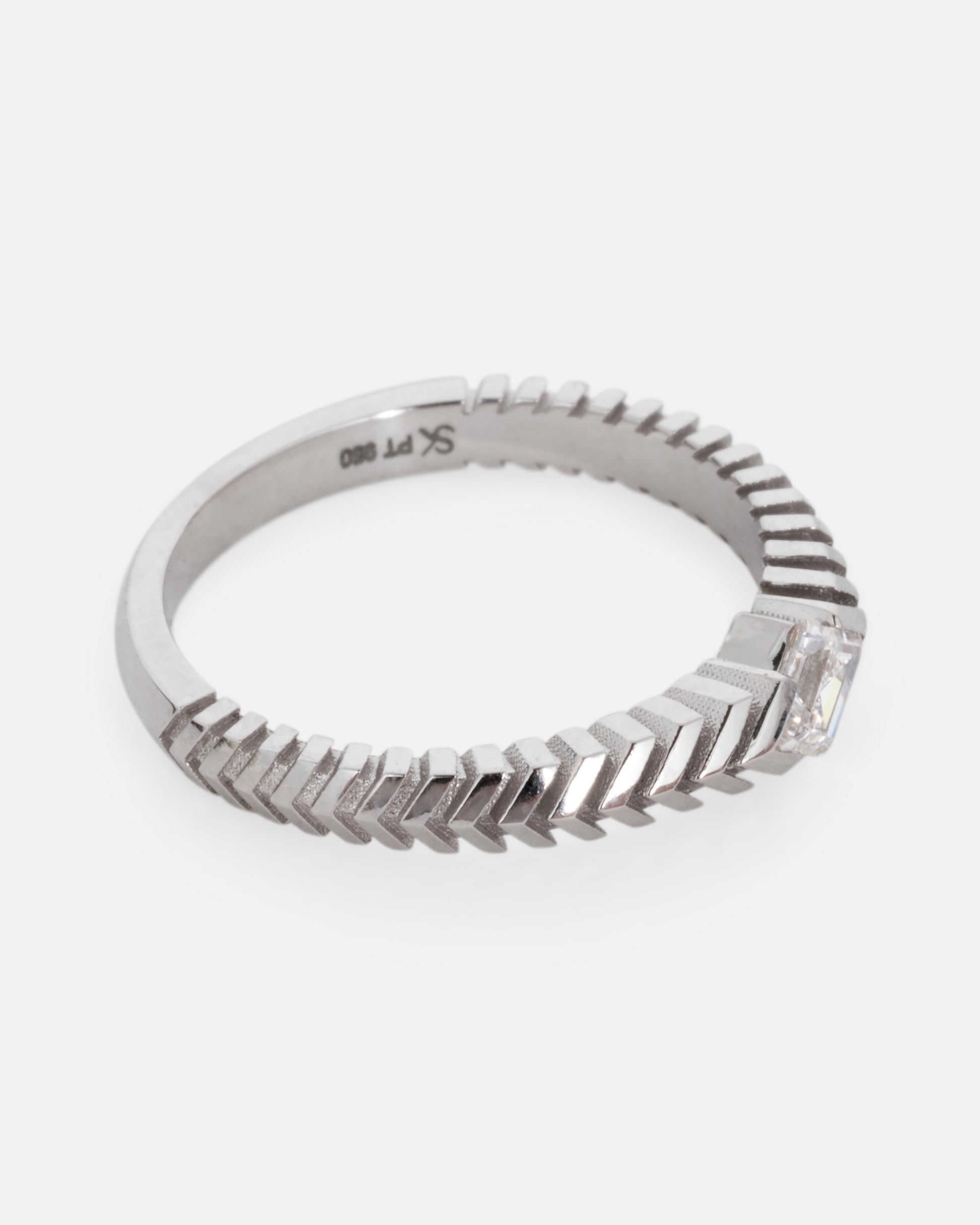 A platinum ring with a 'pleated' motif and lozenge shaped diamond at the center. Shown from the side.