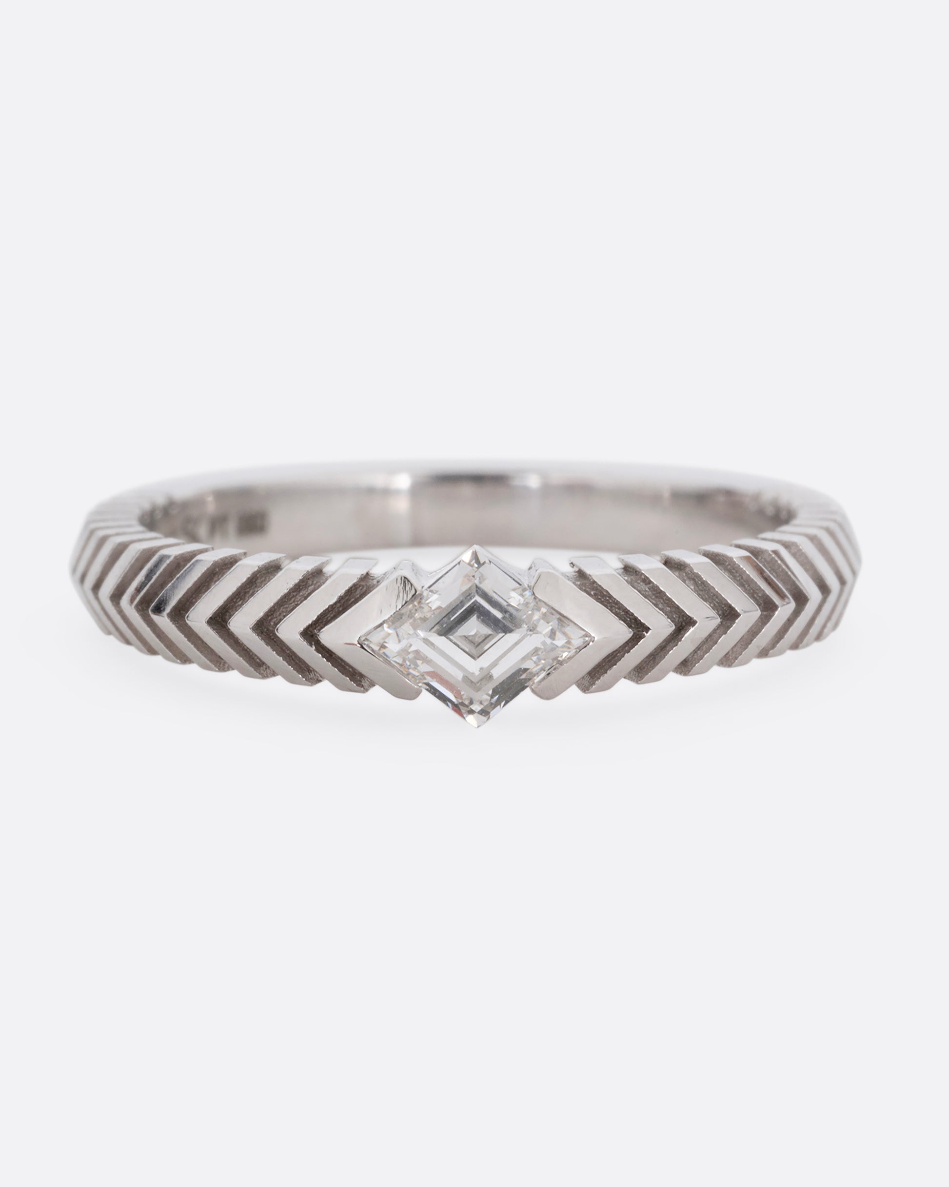A platinum ring with a 'pleated' motif and lozenge shaped diamond at the center. Shown from the front.