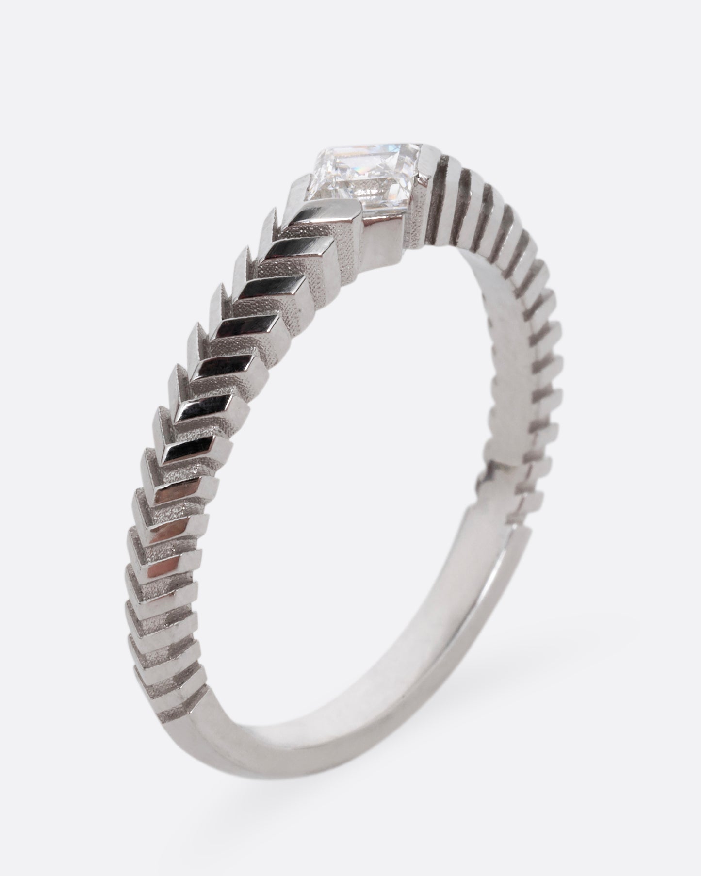A platinum ring with a 'pleated' motif and lozenge shaped diamond at the center. Shown standing up from the side.