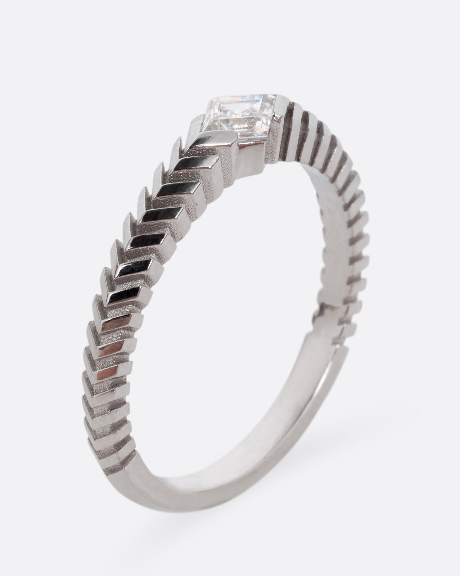 A platinum ring with a 'pleated' motif and lozenge shaped diamond at the center. Shown standing up from the side.