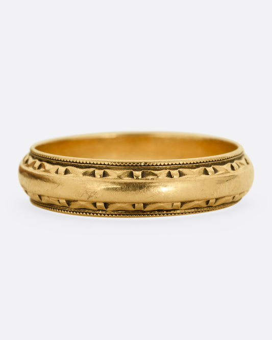 A yellow gold ring with a subtle geometric pattern on its edges. Shown from the front.