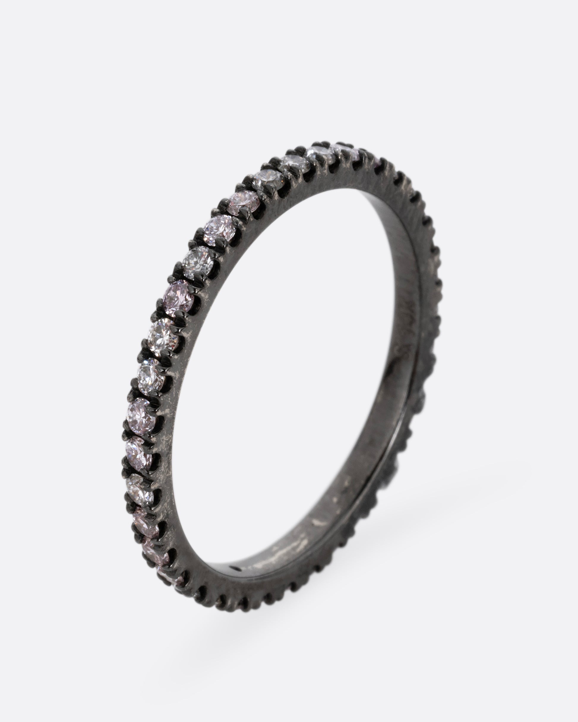 A white gold rhodium plated eternity band with pink, gray, and white diamonds. Shown standing up from the front.