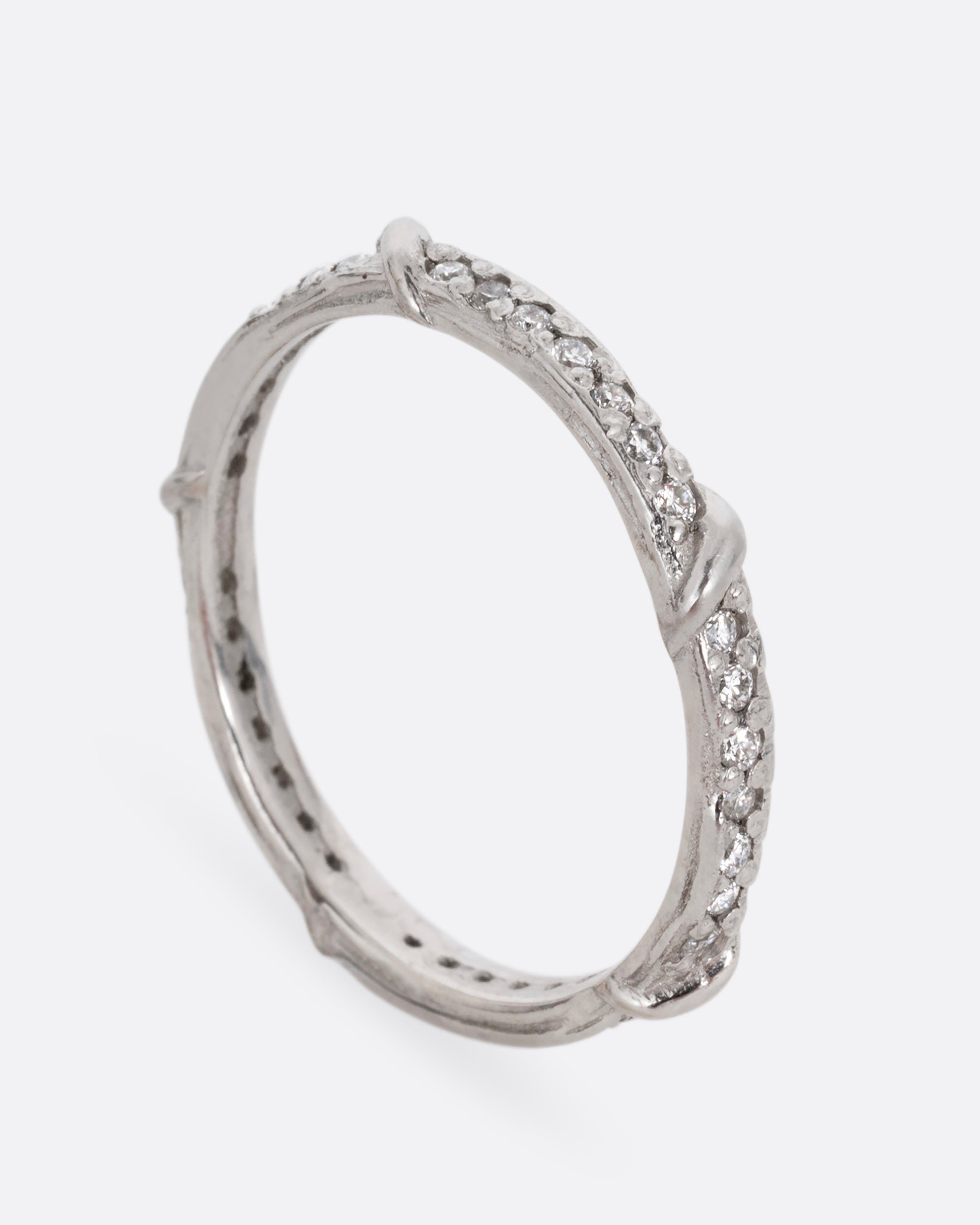 A platinum eternity band with vine detailing and brilliant white diamonds. Shown standing up from the side.